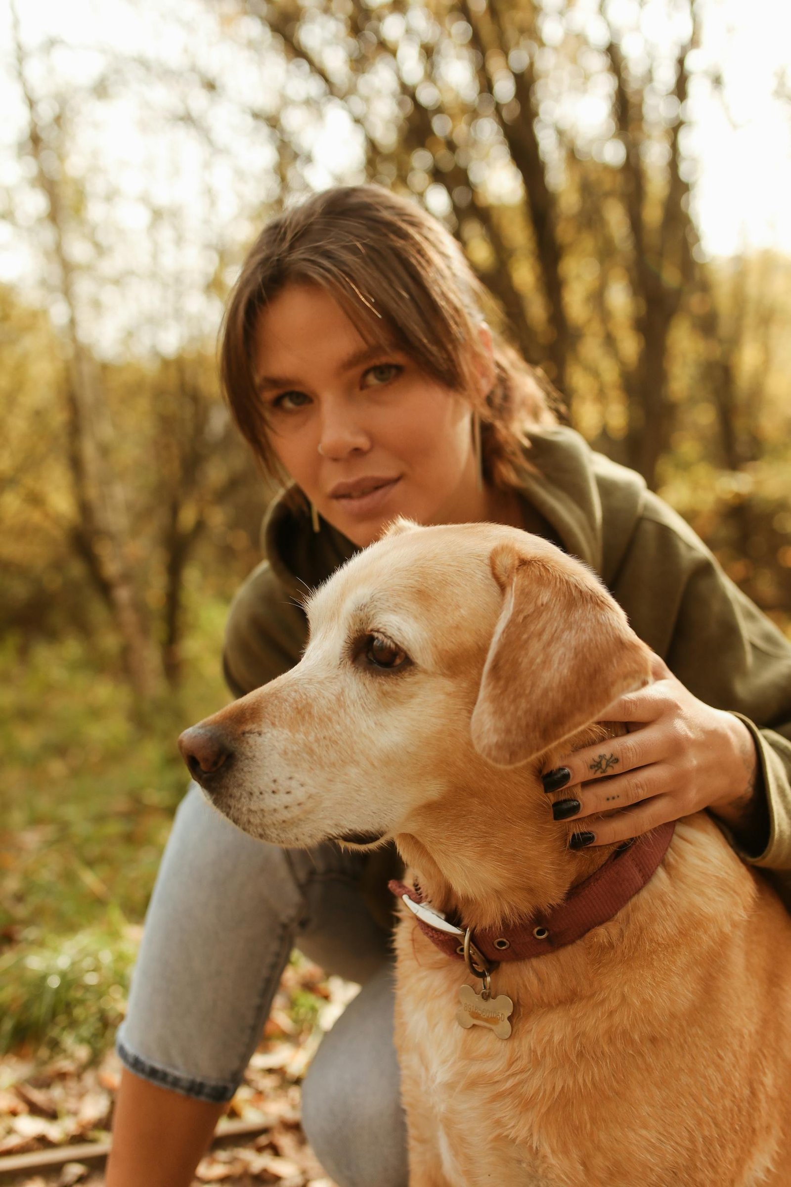 A woman in a green sweater with a Labrador Retriever, enjoying the autumn outdoors.